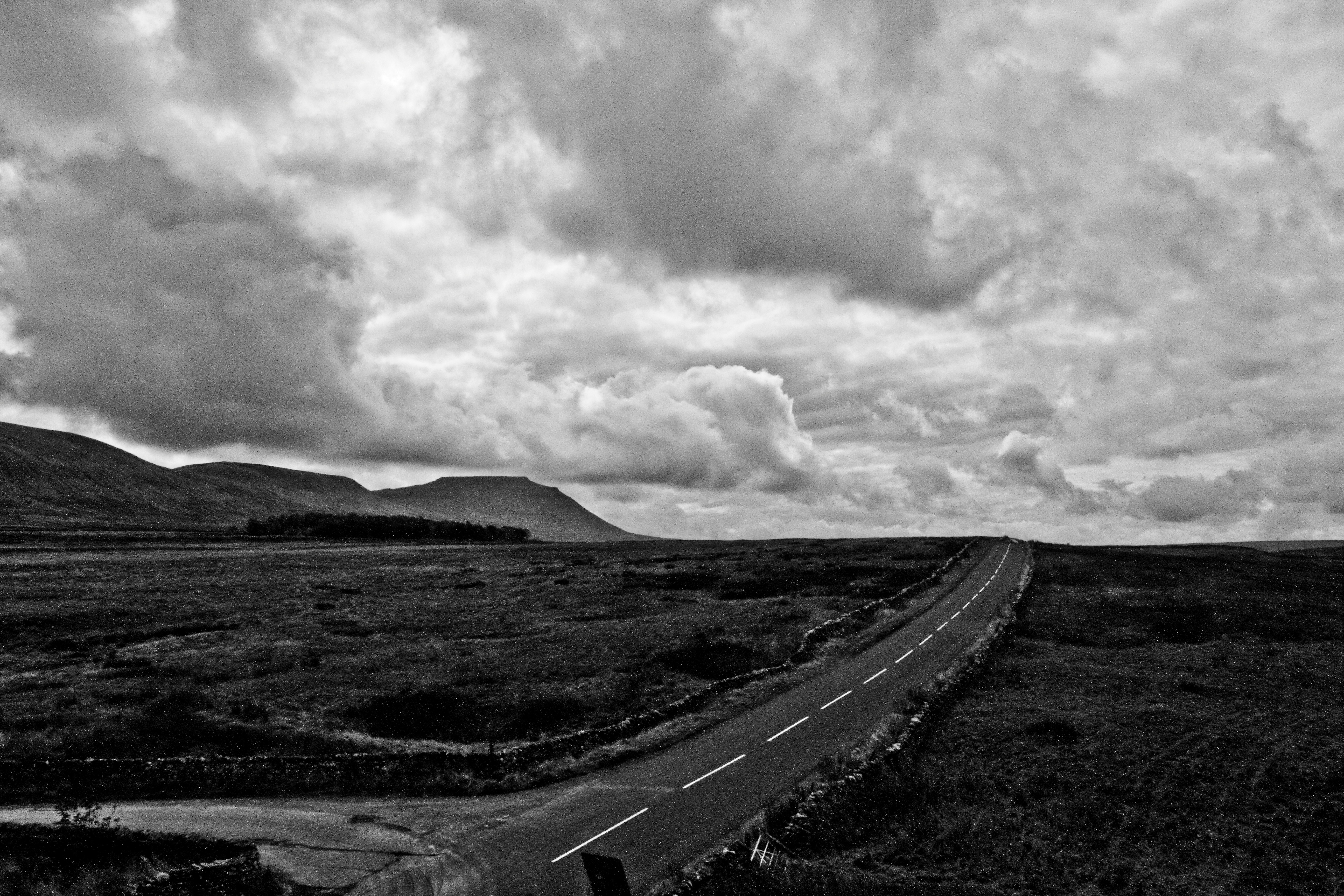 grayscale photo of road under cloudy sky